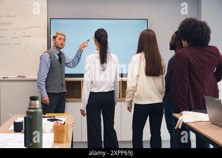 young Latin Man explaining to his colleagues in the office, he is talking to his colleagues standing in front of the blank screen, education concept. Stock Photo