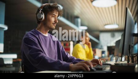 Portrait of a Stylish Male Student Working on His University Project on a Desktop Computer. Young Handsome Man Studying a Course Online in a Quiet Public Library with Bookshelves with Books Stock Photo