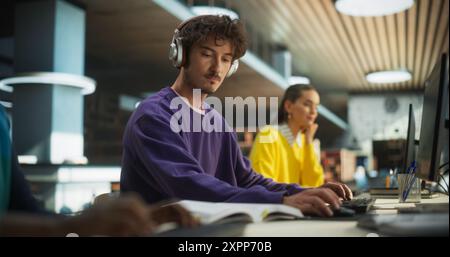 Portrait of a Smart Male Working on a Computer with a Group of University Students. Young Man Wearing Headphones, Doing Homework Assignment and Preparing for STEM Exams in a College Library Stock Photo