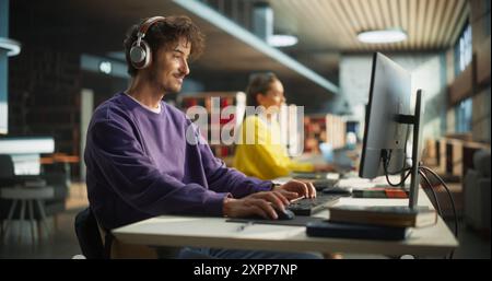 Excited Young Male is Focused on Creating a College Presentation for Class Assignment, Using Online Office Software on Desktop Computer in a Public Library Space with Other Students Stock Photo