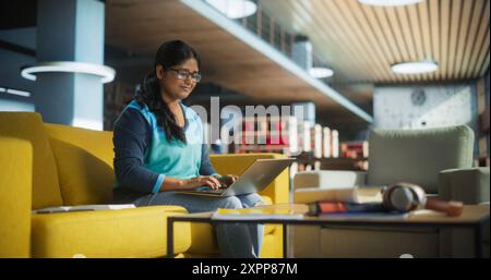 Smart Indian Female Student in Glasses Working on Software Development Assignment in a Quiet Public Library. Young South Asian Woman Using Laptop Computer and Preparing for Examination in College Stock Photo