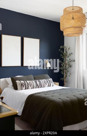 A bedroom detail with two blank frames on a dark blue accent wall and a bohemian rattan hanging light. Stock Photo