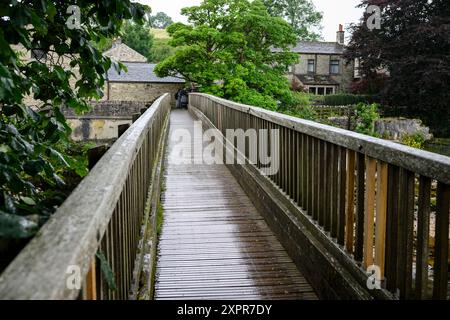 Grassington Yorkshire UK-27 July 2024. Charming wooden footbridge leading to a quaint stone building in a lush, green rural village. Stock Photo