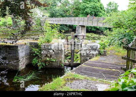 Grassington Yorkshire UK-27 July 2024. Historic wooden bridge over a serene river with lush greenery and old stone structures. Stock Photo