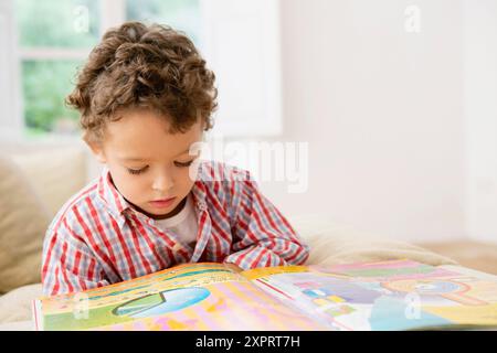 Four year old boy reading a book on the sofa Stock Photo