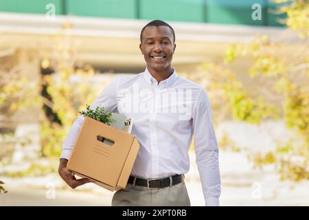 Young Man Smiling While Carrying Box of Plants Outdoors Stock Photo