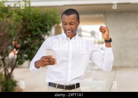 Excited Young Man Celebrating While Checking His Smartphone Outdoors Stock Photo