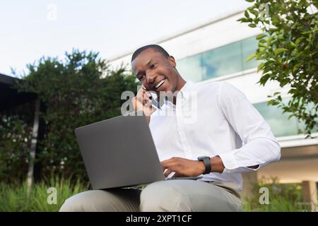 Young Man Working Remotely on Laptop While Talking on Phone Stock Photo