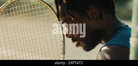 African-American man with dreadlocks holding a tennis racket in a focused and determined manner. Stock Photo
