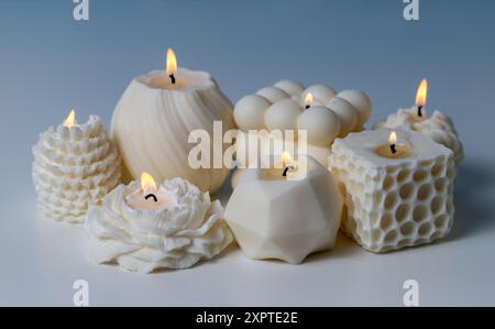 Burning candles of different shapes. White natural scented wax handmade candle on the table. Holiday background in pastel colors. Stock Photo