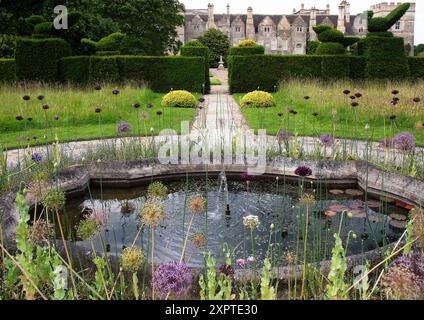 Lily-pond and fountain in Grimsthorpe Castle gardens surrounded by mixed alliums, opium poppies, Dutch iris and forget-me-nots; Stock Photo