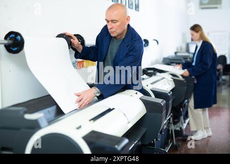 Service man uses plotter and checks functionality in printing shop Stock Photo
