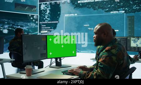 Military expert handles satellite cctv data next to mockup screen, working in a base of operations with high tech gear to support important defense missions. Coordinates strategic tactics. Camera B. Stock Photo