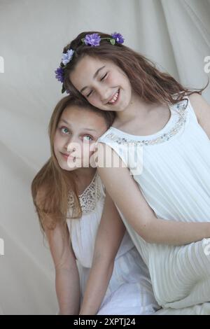 two cheerful preteen girls wearing white dresses on light background Stock Photo