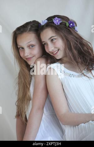 two cheerful preteen girls wearing white dresses on light background Stock Photo