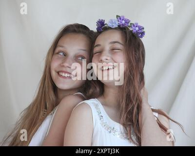 two cheerful preteen girls wearing white dresses on light background Stock Photo