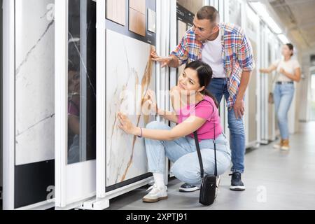 Couple exploring tile samples on sliding display stand in showroom Stock Photo