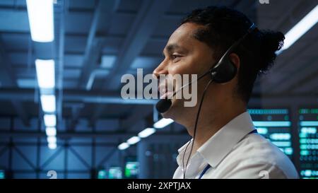 System administrator in data center managing and maintaining databases, ensuring data integrity, security and availability. Indian man updating server farm supercomputers systems, camera B Stock Photo