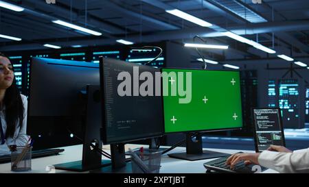 System administrator in data center installing software on isolated screen PC, troubleshooting issues. Admin uses mockup computer in server hub, establishing performance benchmarks, camera B Stock Photo