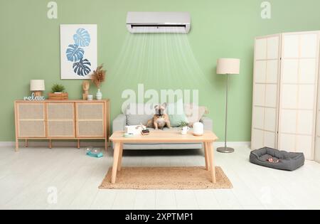 Cute french bulldog sitting on sofa in room with operating air conditioner Stock Photo