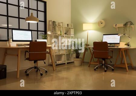Stylish workplaces of programmer with modern computers and glowing lamps in office Stock Photo