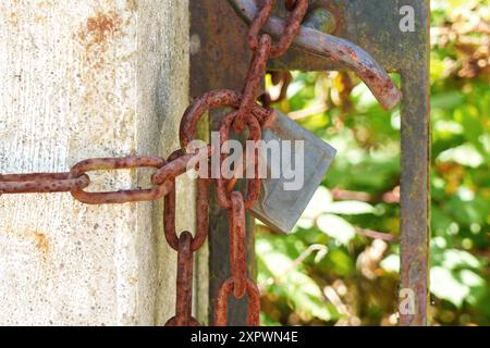 Old corroded padlock on a rusty chain hanging on a closed ancient garden gate Stock Photo