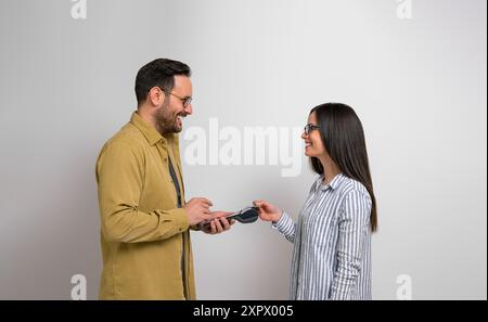 Side view of smiling female customer tapping credit card on card reader machine held by male cashier against background. Man and woman recommending ca Stock Photo