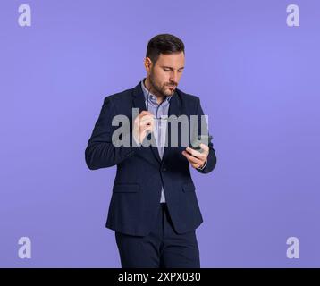 Serious pensive young business professional holding eyeglasses and reading e-mails over smart phone. Male executive with spectacles thinking while doi Stock Photo