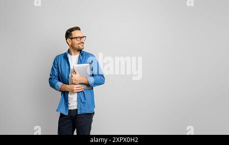 Smiling male professional holding digital tablet looking away thoughtfully against white background Stock Photo