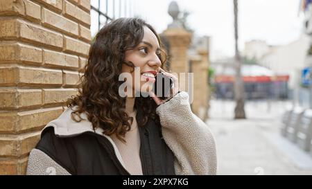 Smiling mixed-race woman talking on a smartphone in a city environment, showcasing urban lifestyle and communication. Stock Photo