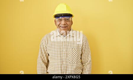 A cheerful middle-aged hispanic man wearing a hardhat against a yellow background exudes professionalism and approachability. Stock Photo