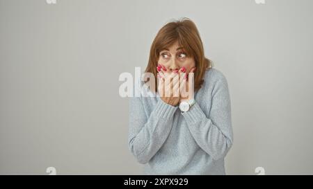 Surprised mature woman covers mouth with hands against isolated white background, expressing shock Stock Photo