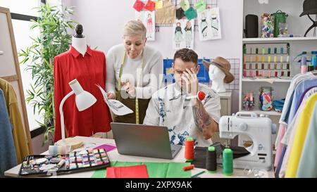 In a tailor shop, a man and a woman, both designers, collaborate over fashion sketches by a sewing machine. Stock Photo