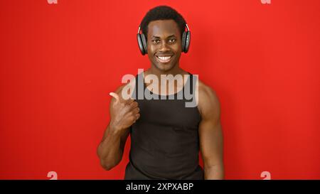 A smiling african american man with headphones gesturing thumbs up against a red background. Stock Photo