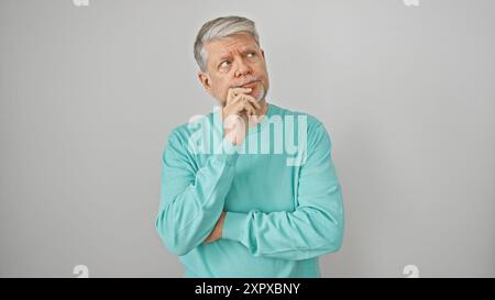 A thoughtful mature man with grey hair wearing a teal sweater poses against a white background, embodying wisdom and contemplation. Stock Photo