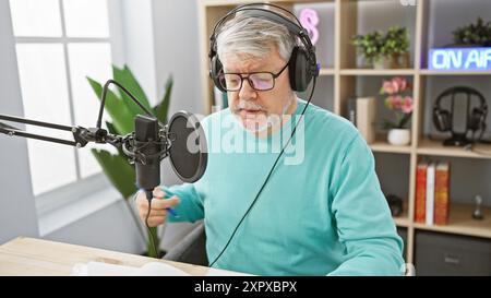 Middle-aged man with headphones speaks into microphone in a bright radio studio Stock Photo