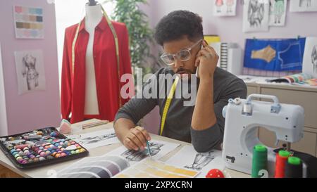 African american male tailor in atelier on phone with fabric swatches and sewing machine Stock Photo