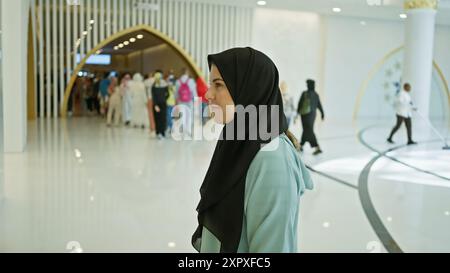 A thoughtful young woman in a hijab stands contemplatively in an ornate abu dhabi mosque, epitomizing islamic culture. Stock Photo