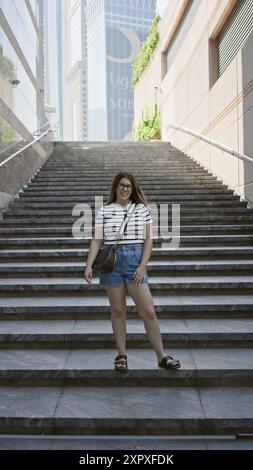 Smiling woman wearing glasses stands on stairs with modern skyscrapers in dubai in the background Stock Photo