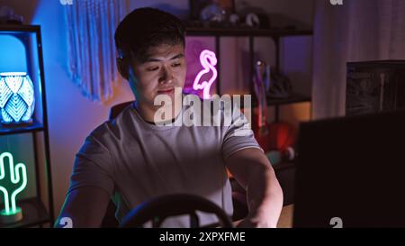 A young asian man enjoys sim racing in a home gaming setup at night, portraying technology and leisure. Stock Photo