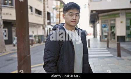 A casual young asian man wearing a jacket stands confidently on an urban city street. Stock Photo