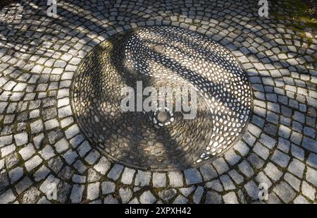 Overhead close-up of a decorative yin-yang pebble mosaic medallion set into cobblestone pavement in the Chinese Garden in Stuttgart, Germany. Stock Photo