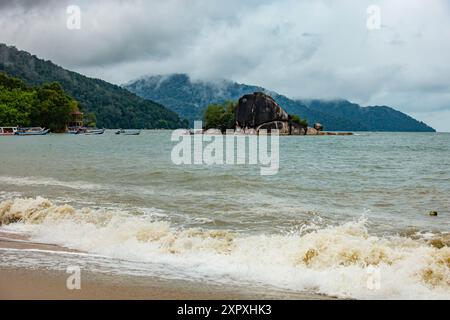 Waves breaking onto Btu Ferringhi beach in Pengang, Malaysia. Low cloud comes over the headland and waves break on the beach. Stock Photo