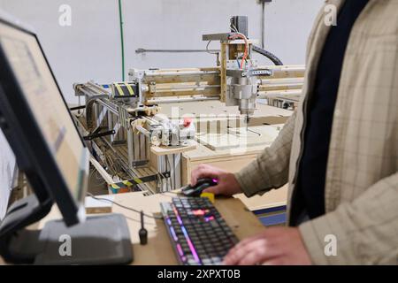 Operator Entering Coordinates on Computer for CNC Machine to Precisely Cut Wooden Pieces Stock Photo