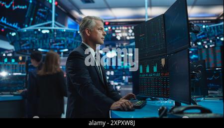 Financial Analyst Using Desktop Computer with Multi-Monitor Workstation with Real-Time Graphs, Financial Reports and Market Charts. Trader Working in a Modern Stock Exchange Business Venture Stock Photo
