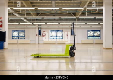 Used green manual pallet jack or forklift on an empty, illuminated factory floor, no people. Stock Photo