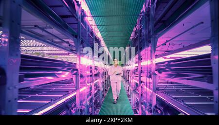 Female Agricultural Scientist Walking in a Vertical Farm Facility Next to Racks with Fresh Natural Crops. Hydroponics Technician Using a Tablet Computer, Studying and Cultivating Plants Stock Photo