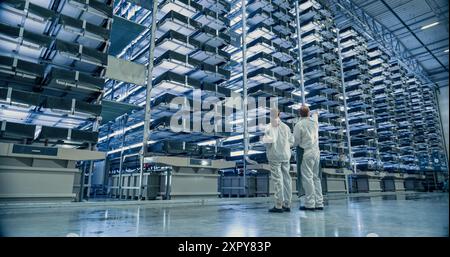 Work at an Advanced Vertical Farm WIth LED Lights. Two Facility Workers Discussing Business, Using Tablet Computer while Monitoring Farming Produce Optimization for Increased Agricultural Yields Stock Photo