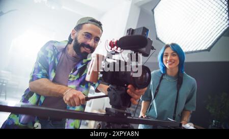 Young Latin Male And Caucasian Female Filmmakers Collaborate In A Modern Studio, Handling Professional Camera Equipment With Enthusiasm And Expertise, Showcasing Teamwork In Creative Media Production. Stock Photo