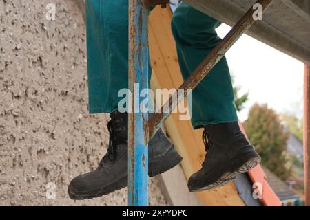 Close-up of the legs of a construction worker sitting on scaffolding Stock Photo